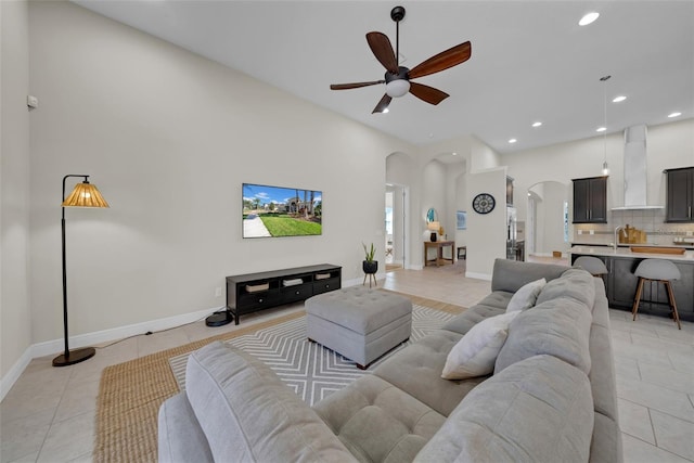 living area featuring arched walkways, light tile patterned floors, recessed lighting, ceiling fan, and baseboards