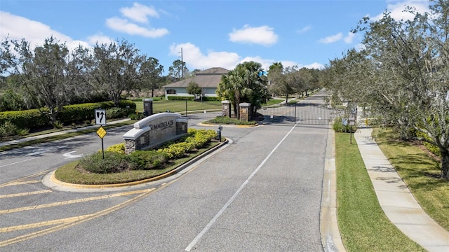 view of road with traffic signs, a gate, sidewalks, a gated entry, and curbs