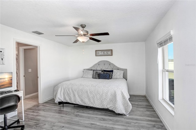 bedroom with visible vents, a textured ceiling, baseboards, and wood finished floors