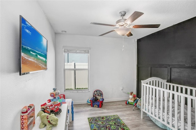 bedroom with a crib, wood finished floors, a ceiling fan, and baseboards