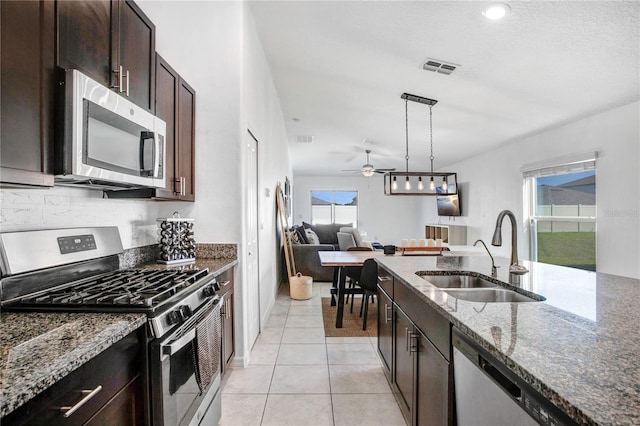 kitchen with light tile patterned flooring, stainless steel appliances, a sink, open floor plan, and dark stone countertops