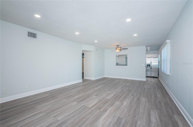 unfurnished living room featuring a textured ceiling, wood finished floors, visible vents, and baseboards