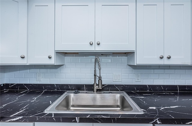 kitchen with decorative backsplash, dark countertops, a sink, and white cabinets