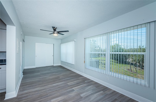 unfurnished room with dark wood-type flooring, plenty of natural light, a textured ceiling, and baseboards