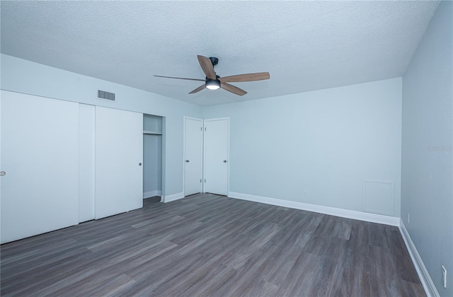 unfurnished bedroom with a textured ceiling, visible vents, baseboards, a closet, and dark wood-style floors