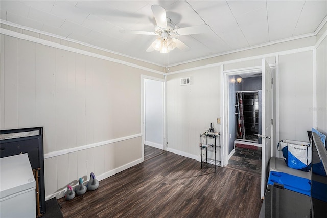 interior space with wood finished floors, a ceiling fan, visible vents, baseboards, and ornamental molding