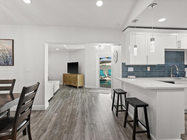 kitchen featuring tasteful backsplash, a breakfast bar, wood finished floors, light countertops, and white cabinetry