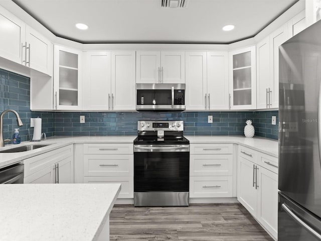 kitchen featuring a sink, white cabinets, appliances with stainless steel finishes, backsplash, and light wood finished floors