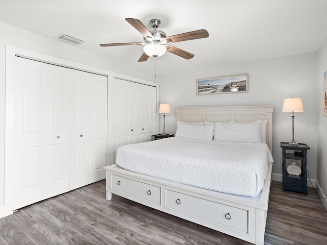 bedroom featuring ceiling fan, visible vents, dark wood-style flooring, and two closets