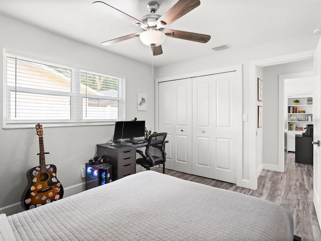 bedroom featuring ceiling fan, wood finished floors, visible vents, baseboards, and a closet