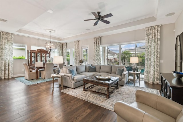 living room with baseboards, ornamental molding, dark wood-style flooring, a tray ceiling, and ceiling fan with notable chandelier