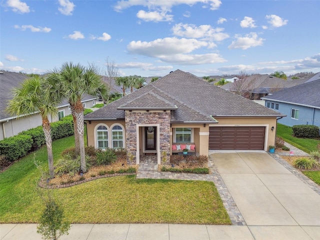 view of front of home with a shingled roof, concrete driveway, an attached garage, stone siding, and a front lawn