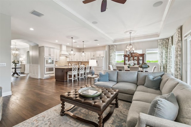 living room featuring arched walkways, dark wood-style flooring, visible vents, a tray ceiling, and crown molding