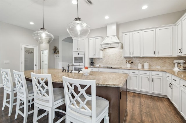 kitchen featuring arched walkways, white double oven, premium range hood, dark wood-type flooring, and a sink