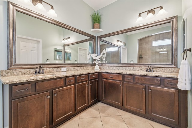 bathroom with double vanity, tiled shower, a sink, and tile patterned floors