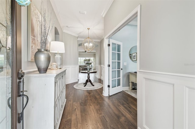 entryway with a chandelier, a decorative wall, wainscoting, dark wood finished floors, and crown molding