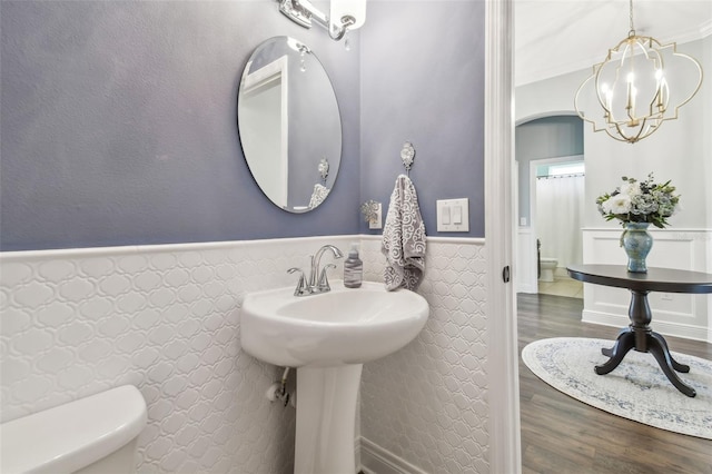 half bathroom featuring a wainscoted wall, a notable chandelier, toilet, and wood finished floors