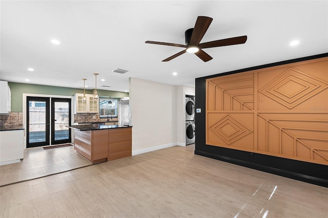 810 22nd St N, Saint Petersburg, FL 33713 - interior space featuring stacked washer and clothes dryer, light wood finished floors, dark countertops, decorative backsplash, and glass insert cabinets