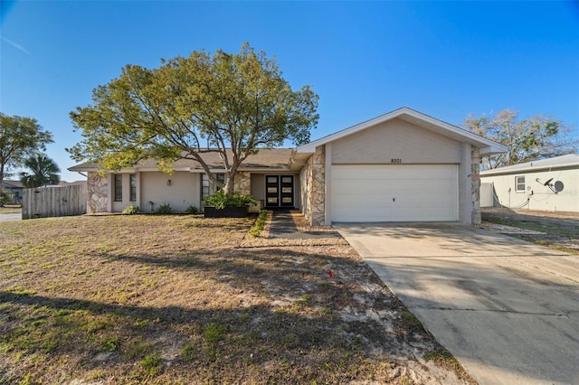 ranch-style house with an attached garage, fence, concrete driveway, stone siding, and stucco siding