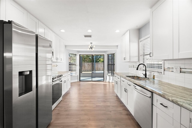 kitchen with visible vents, decorative backsplash, light wood-style flooring, stainless steel appliances, and a sink