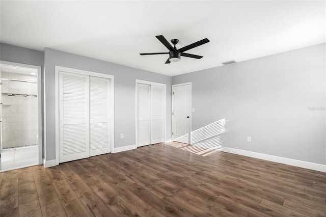 unfurnished bedroom featuring visible vents, dark wood finished floors, baseboards, and two closets