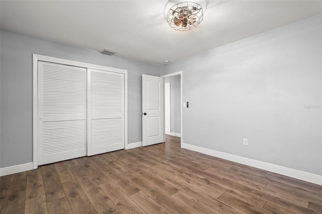 unfurnished bedroom featuring baseboards, a closet, visible vents, and wood finished floors