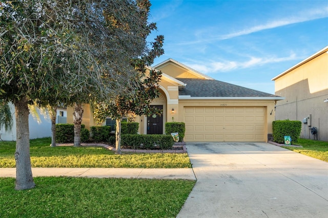 view of front facade with a garage, a shingled roof, concrete driveway, a front lawn, and stucco siding