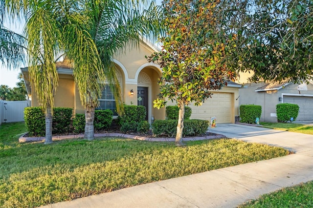 view of property hidden behind natural elements featuring stucco siding, concrete driveway, fence, a garage, and a front lawn