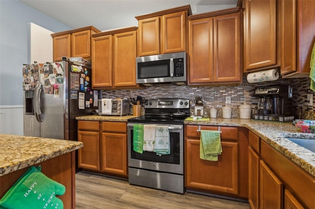 kitchen with appliances with stainless steel finishes, light wood-style floors, light stone counters, and decorative backsplash