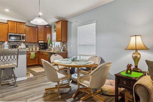 kitchen featuring pendant lighting, brown cabinets, light wood finished floors, stainless steel appliances, and tasteful backsplash