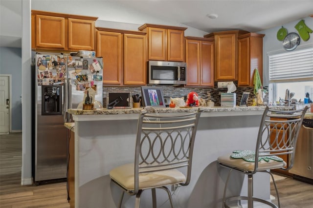 kitchen featuring light wood-type flooring, stainless steel appliances, decorative backsplash, and a kitchen breakfast bar