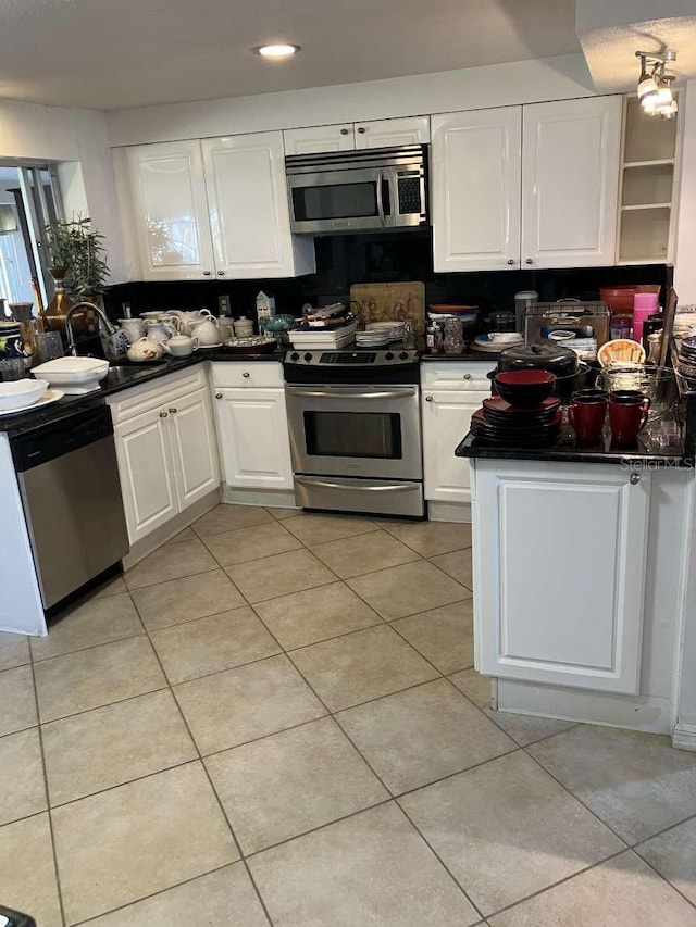 kitchen with dark countertops, light tile patterned floors, white cabinetry, and appliances with stainless steel finishes