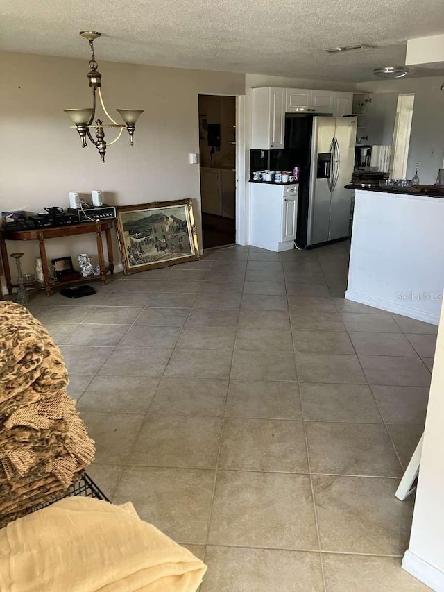 interior space featuring light tile patterned floors, dark countertops, white cabinets, a textured ceiling, and stainless steel fridge with ice dispenser