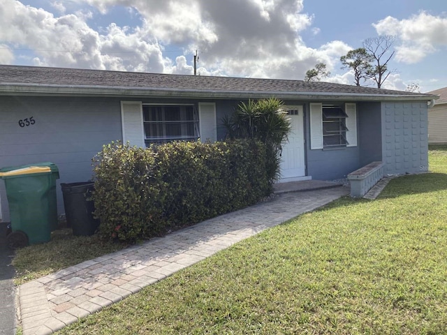 ranch-style house with a shingled roof, concrete block siding, a front lawn, and a garage