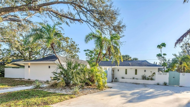 ranch-style home with concrete driveway, fence, a gate, and stucco siding