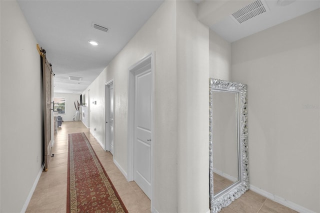 hall featuring a barn door, visible vents, baseboards, and light tile patterned flooring