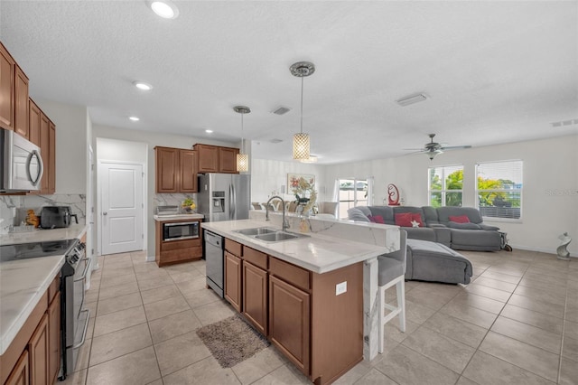 kitchen with a sink, appliances with stainless steel finishes, backsplash, brown cabinets, and a kitchen bar