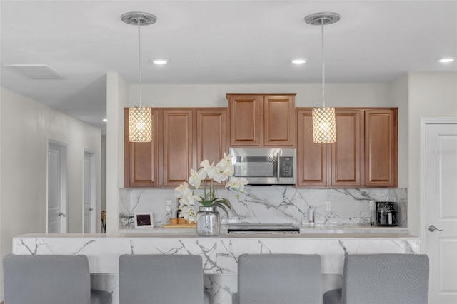 kitchen with decorative light fixtures, stainless steel microwave, visible vents, decorative backsplash, and brown cabinetry