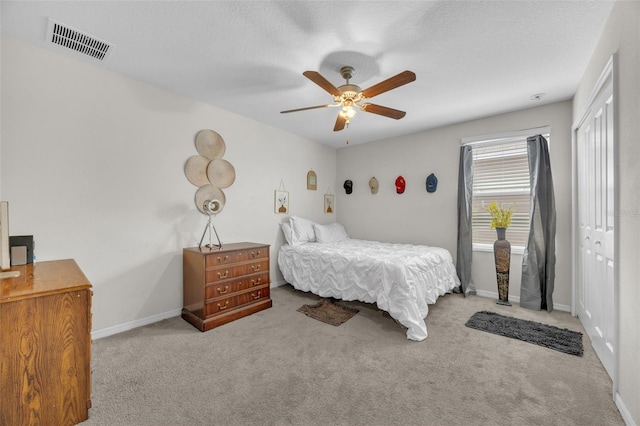 carpeted bedroom with ceiling fan, a textured ceiling, visible vents, baseboards, and a closet