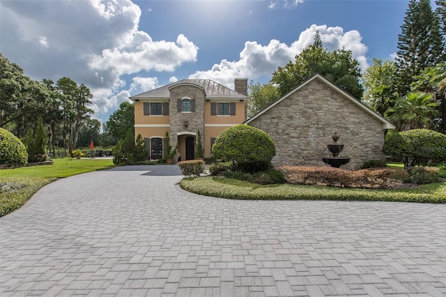 view of front of house with decorative driveway, a chimney, and stucco siding