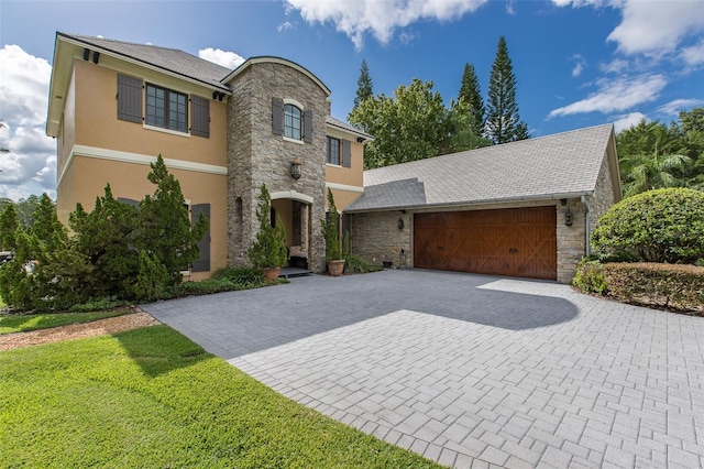 view of front facade with an attached garage, stone siding, decorative driveway, and stucco siding