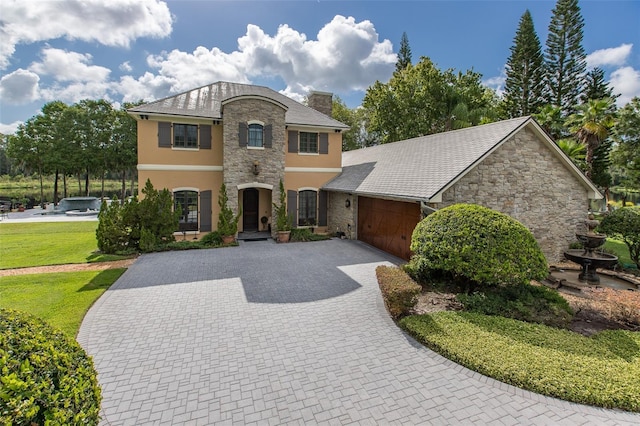 view of front facade featuring a garage, a chimney, decorative driveway, a front lawn, and stucco siding