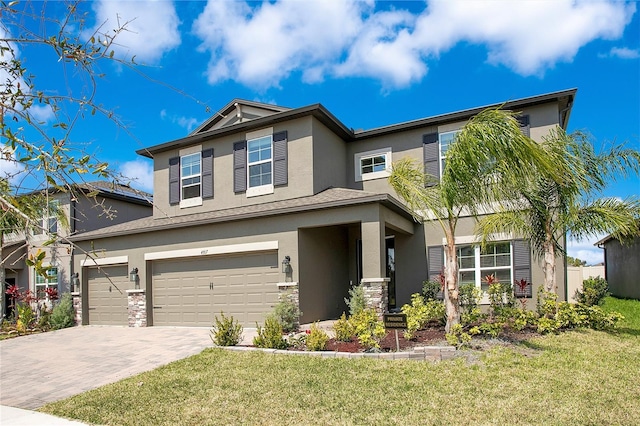 craftsman house with stucco siding, decorative driveway, stone siding, a front yard, and a garage