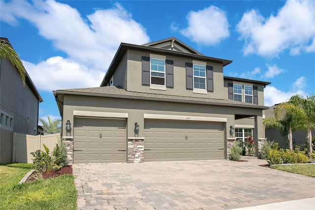 view of front facade featuring decorative driveway, fence, stone siding, and stucco siding