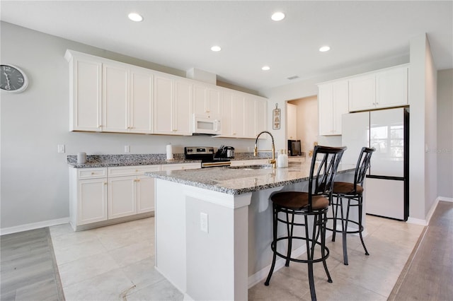 kitchen featuring light stone countertops, a breakfast bar, white cabinets, white appliances, and a sink