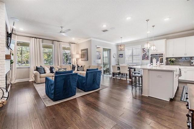 living room with dark wood-style floors, plenty of natural light, crown molding, and ceiling fan