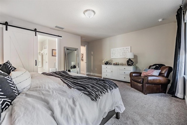 carpeted bedroom with baseboards, visible vents, ensuite bath, a textured ceiling, and a barn door