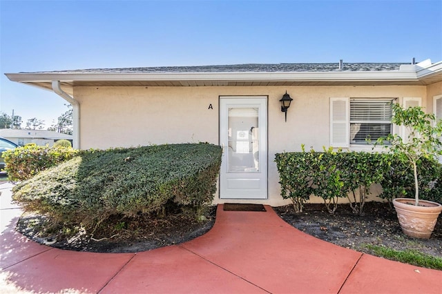 property entrance featuring roof with shingles and stucco siding