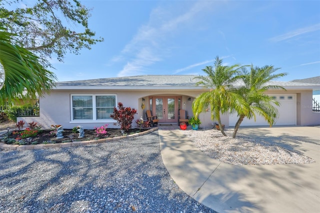 ranch-style house with stucco siding, french doors, an attached garage, and driveway