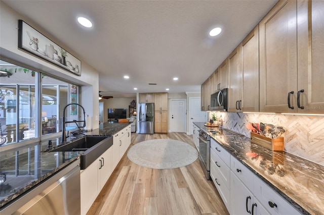 kitchen with dark stone countertops, a sink, stainless steel appliances, light wood-type flooring, and backsplash